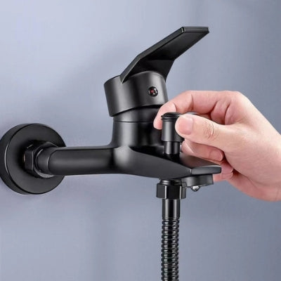Une main tire sur le bouton inverseur du tuyau de la douchette du robinet de baignoire de couleur noir pour faire couler l'eau.