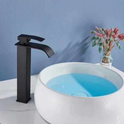 Le robinet pour lavabo noir mat long est debout devant la vasque remplie d'eau. Un joli vase de fleurs est à côté de la vasque.